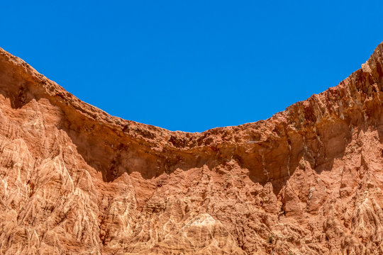View of curved red sandstone cliff with blue sky in Algarve Portugal.