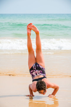 Cute young girl playing on the beach in swimsuit doing a handstand, sea and horizon in the background.