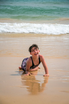 Cute young little girl laughing laying in a swimsuit in the sand on a beach with waves.