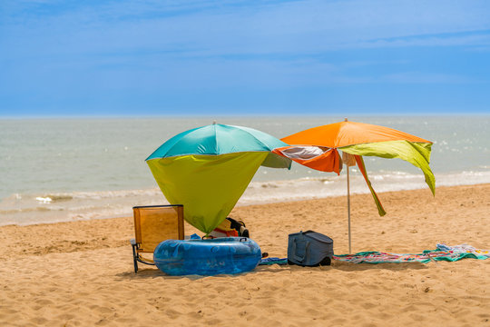 Two colorful sun parasols and a chair at a windy sunny beach in Algarve Portugal.