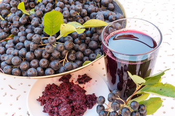 Closeup of fresh juice and jam of ripe black chokeberry (Aronia melanocarpa) in glass and berry in...