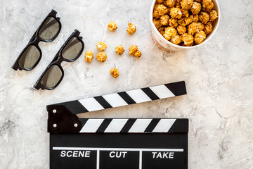 Watching film. Clapperboard, glasses and popcorn on grey stone background top view copyspace
