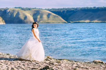 Fototapeta na wymiar Charming bride in white dress walking by the shore of a lake