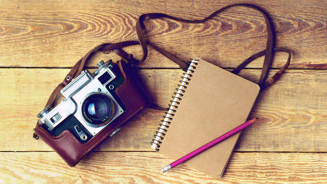 Old retro camera, pencil, kraft paper notebook on vintage rustic wooden planks boards. Education photography courses back to  school concept abstract background. Close up, top view, copy space, toned.