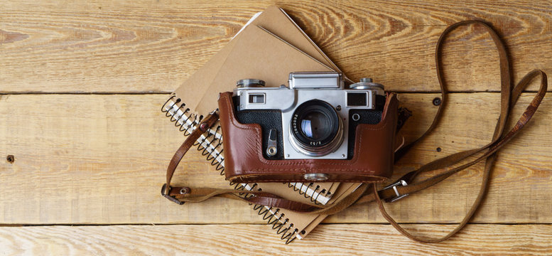 Old retro camera, spiral blank kraft paper notebook on vintage rustic wooden planks boards. Education photography courses back to  school concept abstract background. Close up, top view, copy space.