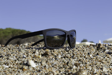 sunglasses on pebble and sky background