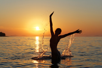 Sylwetka kobiety w wodzie na tle zachodzącego słońca