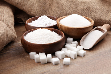 Bowl and scoop with white sand and lump sugar on brown wooden background