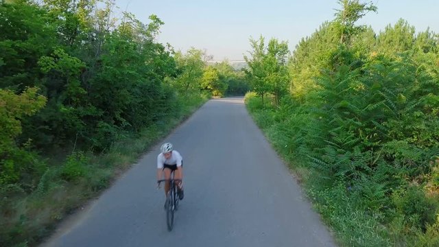 Bicyclist ride bicycle asphalt road in sunny forest helmet sunset drone footage
