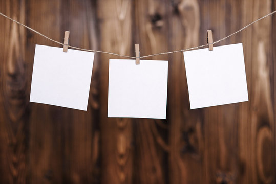 Close up of three white note papers hung by wooden clothes pegs on a brown wooden background