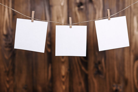 Close up of three white note papers hung by wooden clothes pegs on a brown wooden background