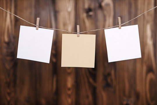 Close up of two white and one beige note papers hung by wooden clothes pegs on a brown wooden background