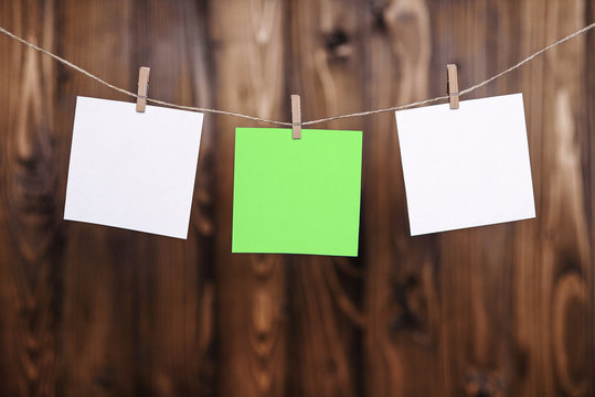 Close up of two white and one green note papers hung by wooden clothes pegs on a brown wooden background