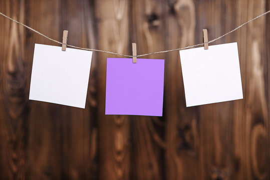Close up of two white and one violet note papers hung by wooden clothes pegs on a brown wooden background