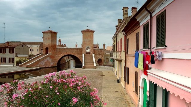 view of picturesque Italian village, where waving colorful clothes are hanging from window to dry overlooking an old bridge, color graded clip