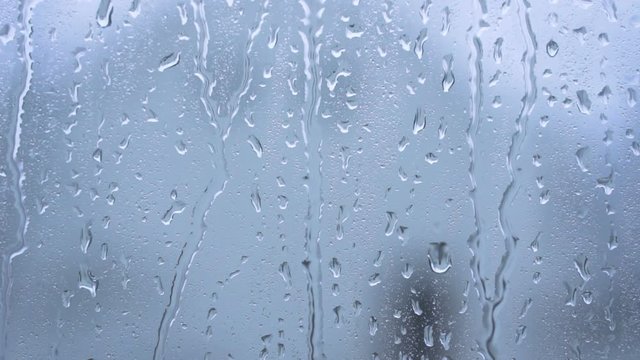 Rain drops running down a window pane. Blue tint blurred background
