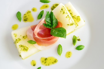 melon prosciutto appetizer decorated with basil leafs and sprinkled with basil, lemon, and olive oil based sauce