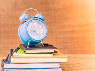 Back to school concept. Retro style of alarm clock on stacks of books with  wooden table background.
