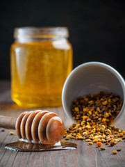 Closeup view of bee pollen and honey dipper with honey on brown wooden table
