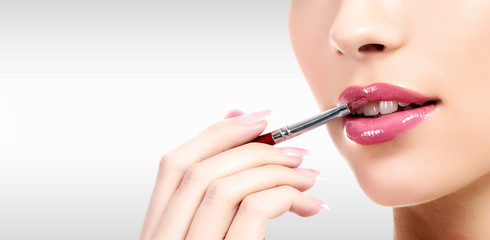 Naklejka premium Closeup shot of woman's lips and hand holding a makeup brush against a grey background with copyspace