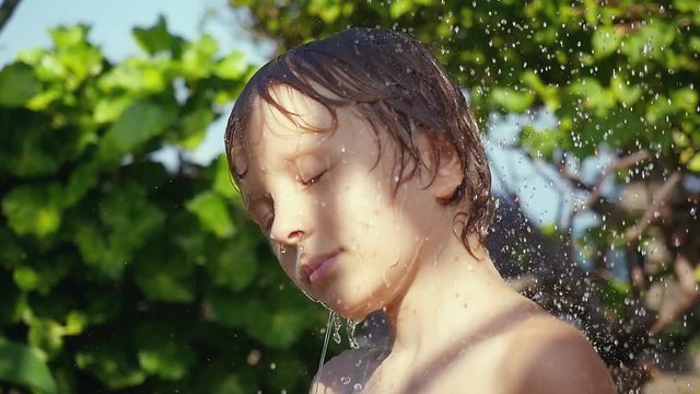 Boy playing with water in the garden, boy has a shower washing hair in slow motion outdoor in summer time. 1920x1080