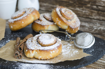  Delicious cinnamon rolls with powdered sugar, metal strainer and cinnamon stick on wooden table. Sweet roll for breakfast. Food backround..