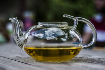 Chinese teapot filled with green tea on a brown wooden table with blurred background