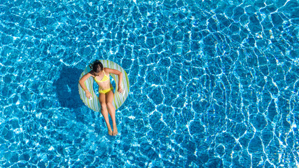 Aerial view of girl in swimming pool from above, kid swim on inflatable ring donut and has fun in...
