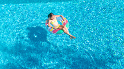 Aerial view of girl in swimming pool from above, kid swim on inflatable ring donut and has fun in water on family vacation
