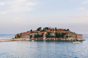 Fototapeta na wymiar Sveti Stefan island landscape near Budva, Montenegro. Evening view of Adriatic sea, St. Stefan luxury fortificated village and sea boats.