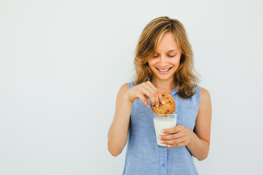 Smiling Young Woman Dunking Cookie In Milk