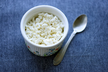 Cottage cheese in a plate with a spoon on a table with a blue tablecloth. Healthy food.