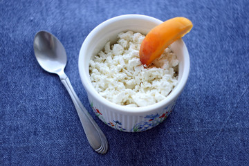 Food. Cottage cheese in a plate, a peach and a spoon on a table with a blue tablecloth.