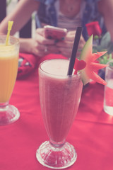 Iced watermelon juice glass on a red table in restaurant and cafe interior. Tropical island of Bali, Indonesia. Woman with smartphone on a background.