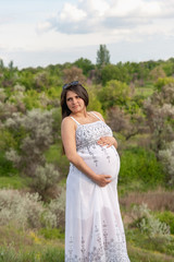 Fototapeta na wymiar Pregnant woman in white dress, resting on a flowering meadow in summer