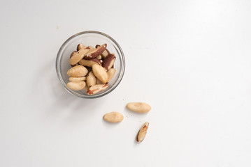 High angle view of brazil nuts in small glass dish and scattered on white table