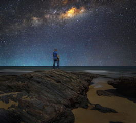 Landscape with Milky Way. Night sky with stars and silhouette of a standing man on the rock at beach.
