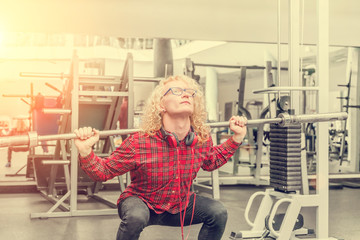 Curly blonde guy in a red shirt with a barbell on the shoulders in the sunlight