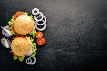 Hamburger with cheese, meat, tomatoes and onions and herbs. On Wooden background. Top view. Free space.