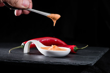 dipping a spoon in hot chili sauce in sauceboat on dark stone background, selective focus