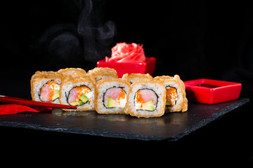 Traditional Japanese cuisine. Selective focus on sushi rolls with salmon, cream cheese, rice, cucumber, caviar and raw meat on dark background, near ginger