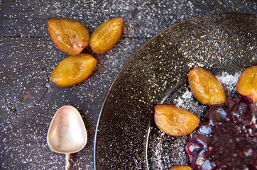 Cool purple jelly with fresh fruits and powder decorated with plums and silver vintage spoon on a dark brown plate on black wooden background. Close up