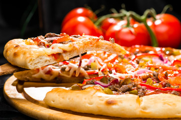 selective focus on piece of appetizing Italian pizza with meat, chili pepper, tomato sauce, pickled cucumbers and mustard on wooden board on dark background, close-up
