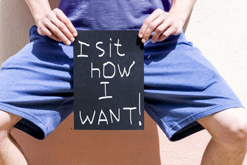 a man holds a banner reading "I sit as I want"