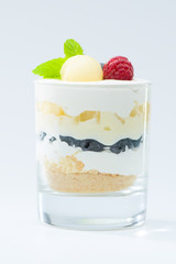 sweet Italian Tiramisu dessert in a glass with raspberries, blueberries, mint and mascarpone on light background