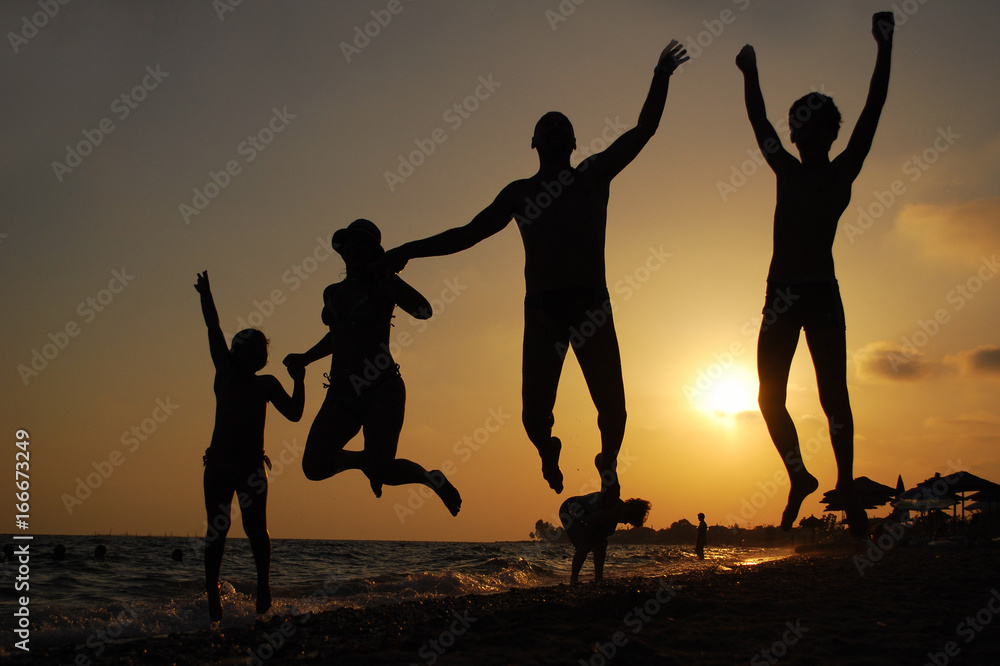 Wall mural family jumping on a beach at sunset. happy family on the sea. summer vacation concept