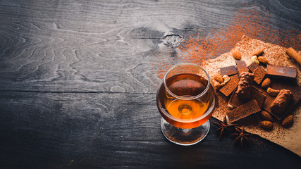 A glass of brandy. Whiskey. Assortment of chocolates. Wooden on the black surface. Top view.