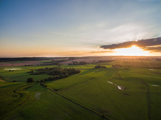 
aerial view of a beautiful sunset with sunbeams above green agricultural fields in the summer