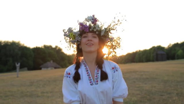 Girl walking in meadow wearing flower circlet and ethnic outfit at sunset in nature.