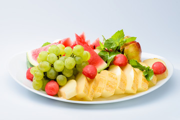 classic summer Italian food. Beautifully decorated fruit platter with watermelon, melon, apricot and grapes on a white plate, light background